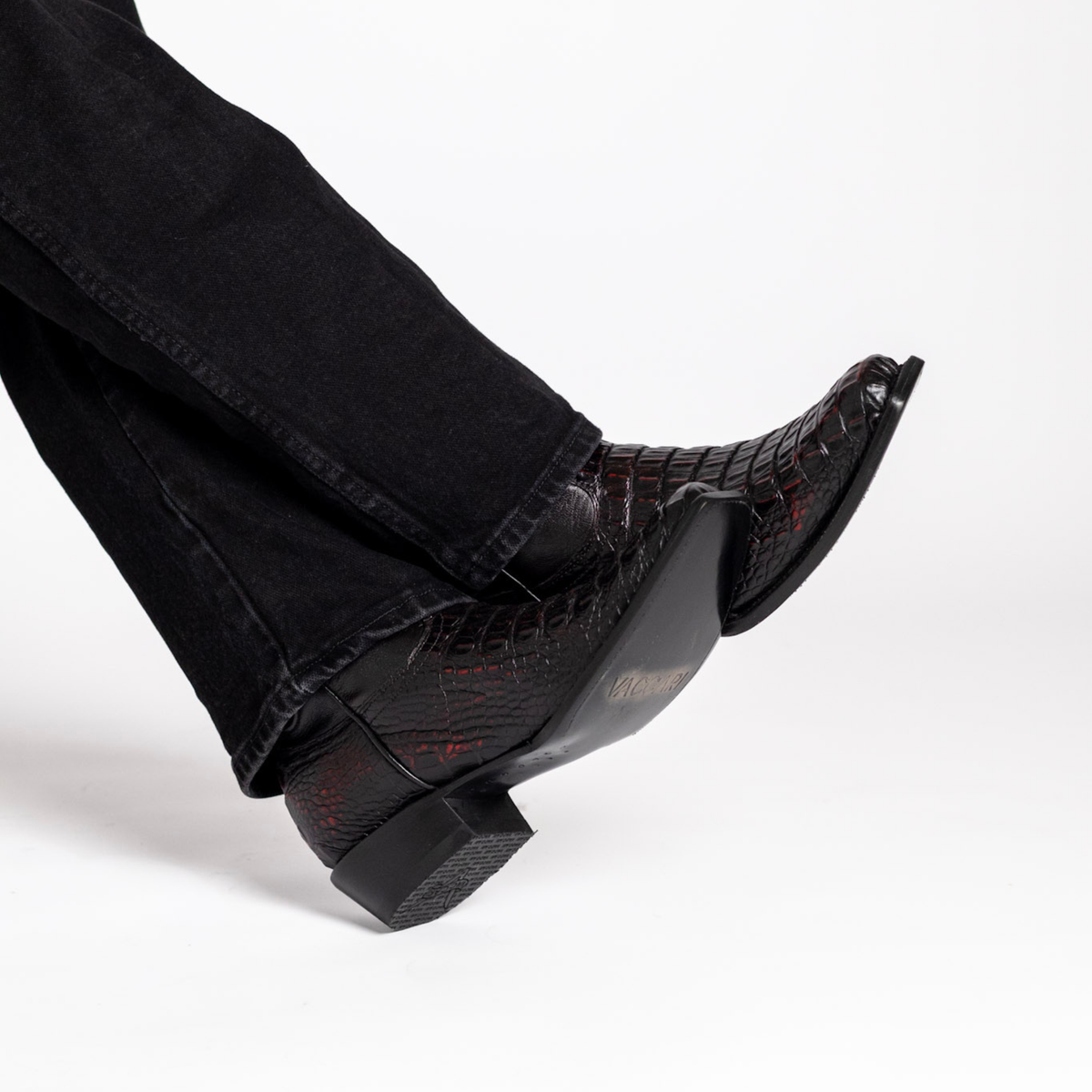 Black cowboy boot near ground with red stitched pattern on toe and low block heel.