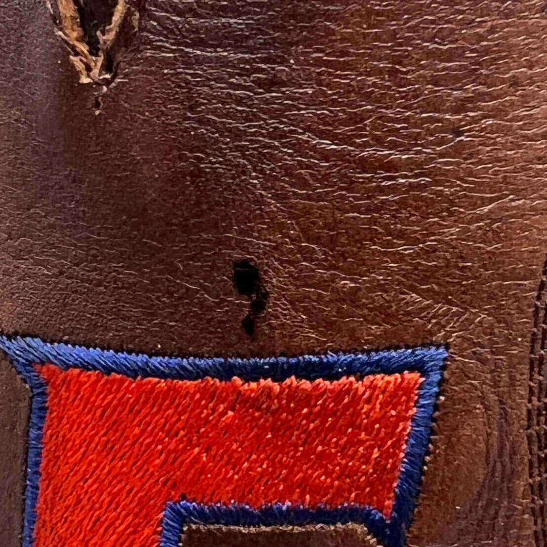 Brown leather boot close-up of red-and-blue embroidered letter with worn thread