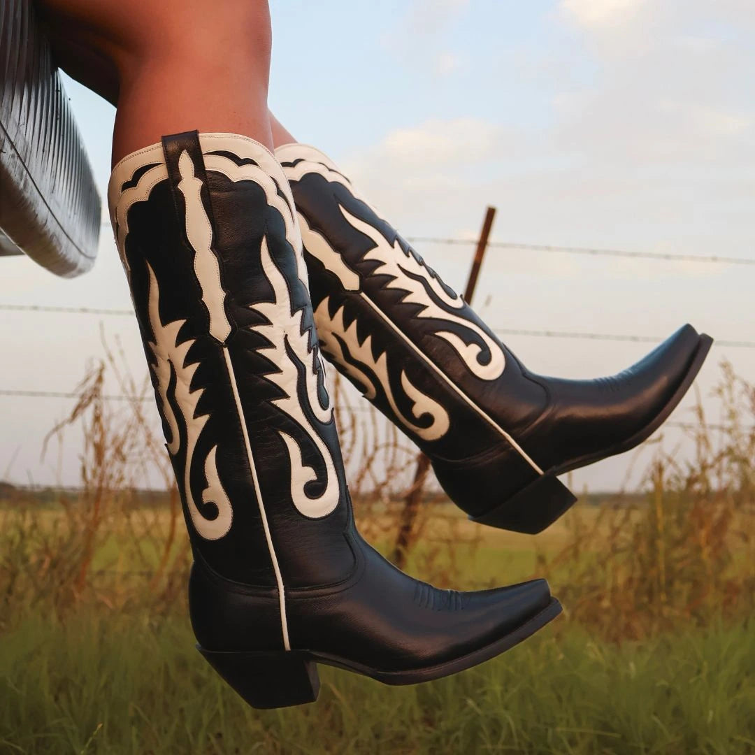 Cowboy boots with black leather and ornate cream scroll embroidery, side view
