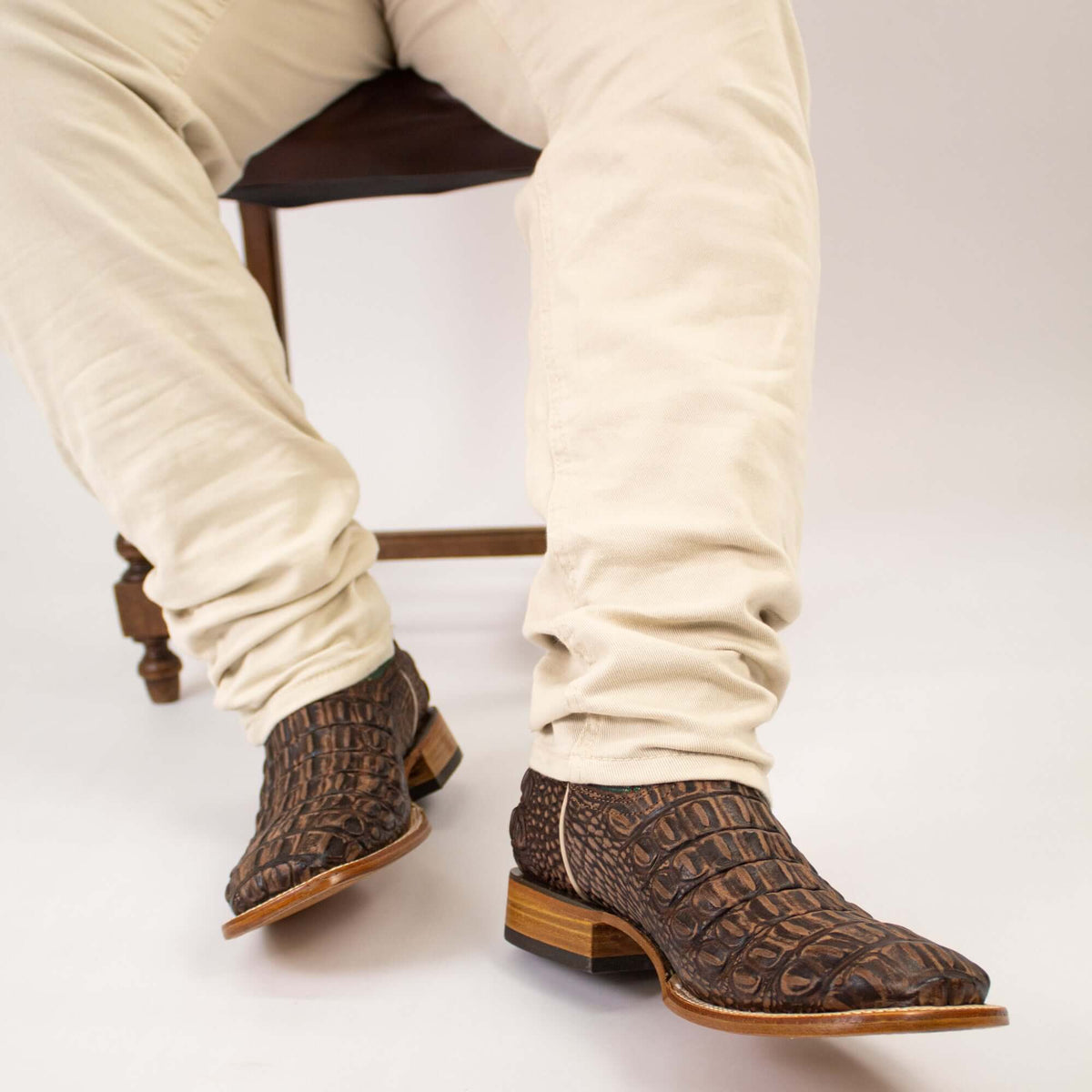 Brown cowboy boots with textured finish worn with light beige pants, side angle view.