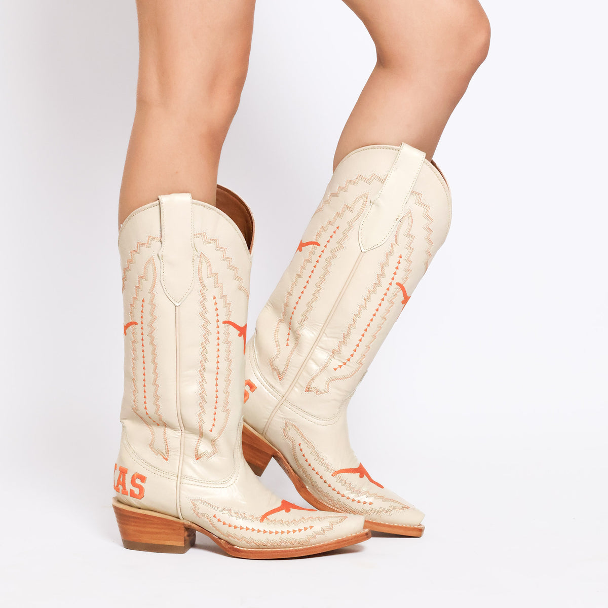 Cowboy boot pair on legs wearing white boots with orange longhorn stitching and low heel.