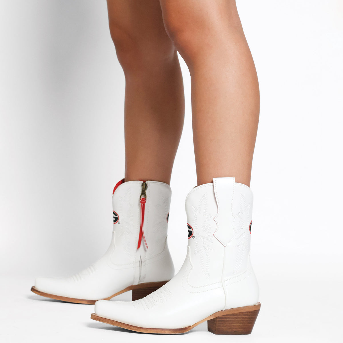 White cowboy boots with red pull tassels, stitched seams, and block heel