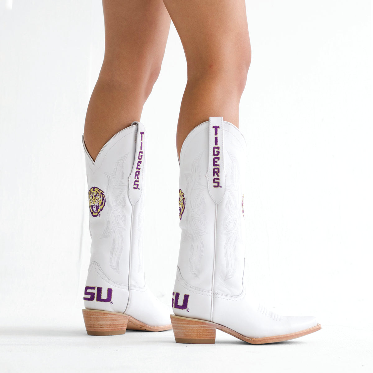 White cowboy boots with purple Tigers side text, colorful emblem, tan heel.