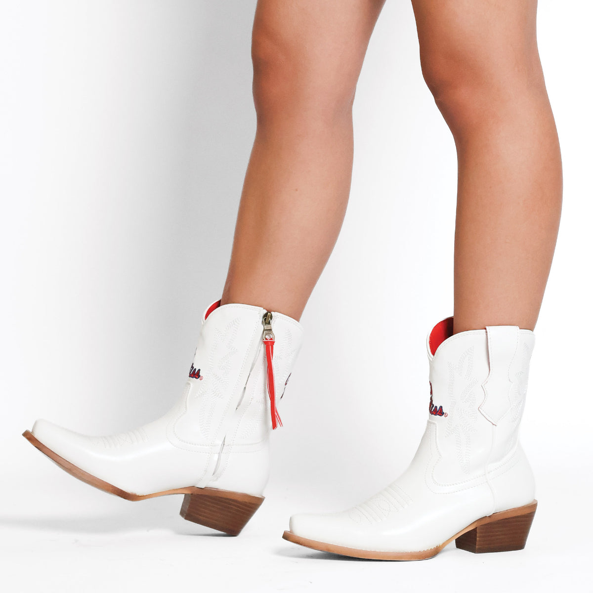 White cowboy boots side view with red trim, tassel zipper, brown stacked heel