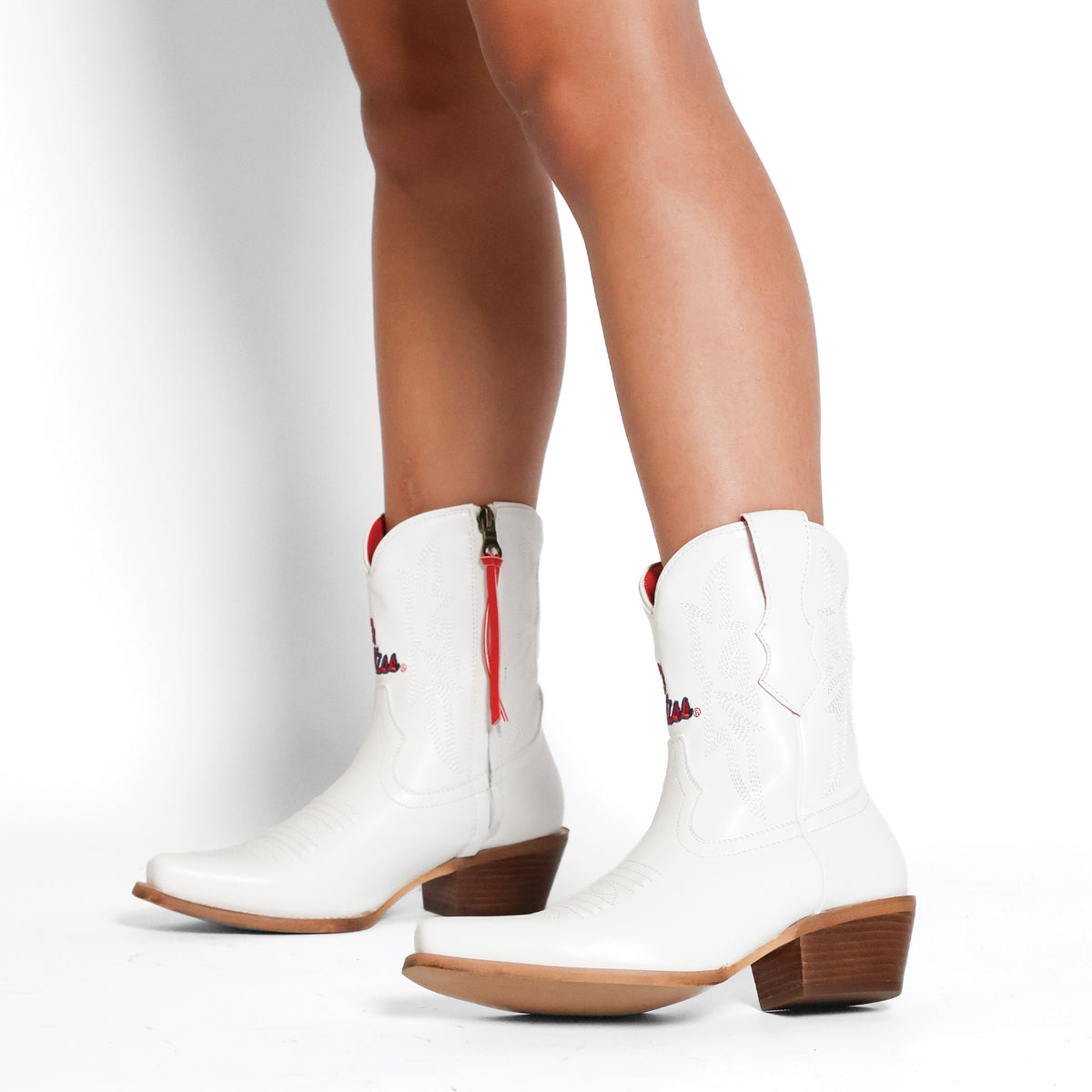 White cowboy boots with red tassel zipper and stitched detail, brown stacked heel