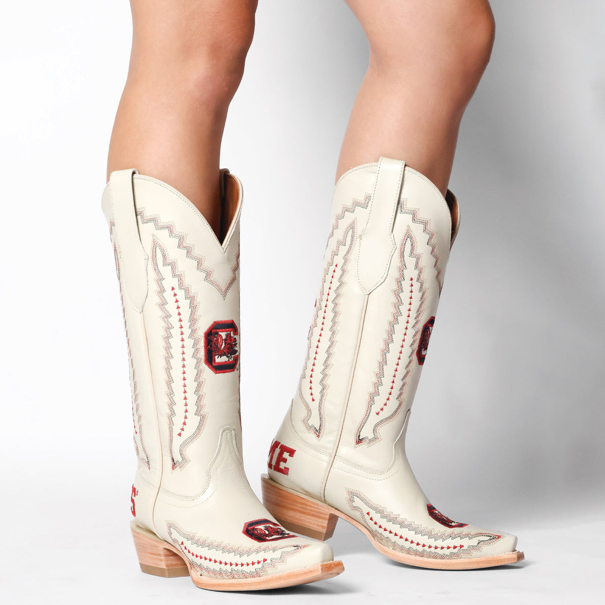 Cream cowboy boots with red emblem patches, stitched zigzag trim, and block heels