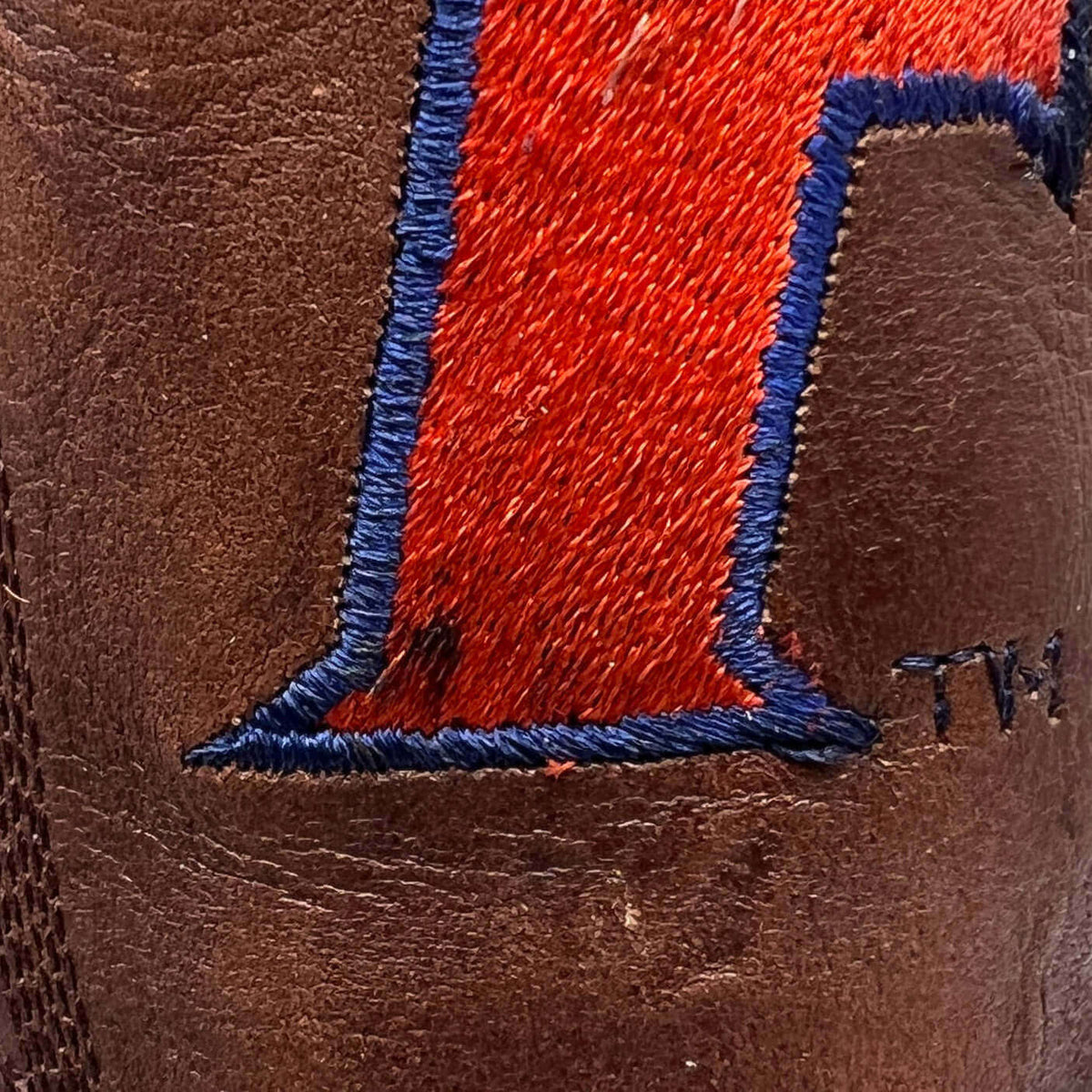 Brown leather boot with red-and-blue letter embroidery and visible stitching