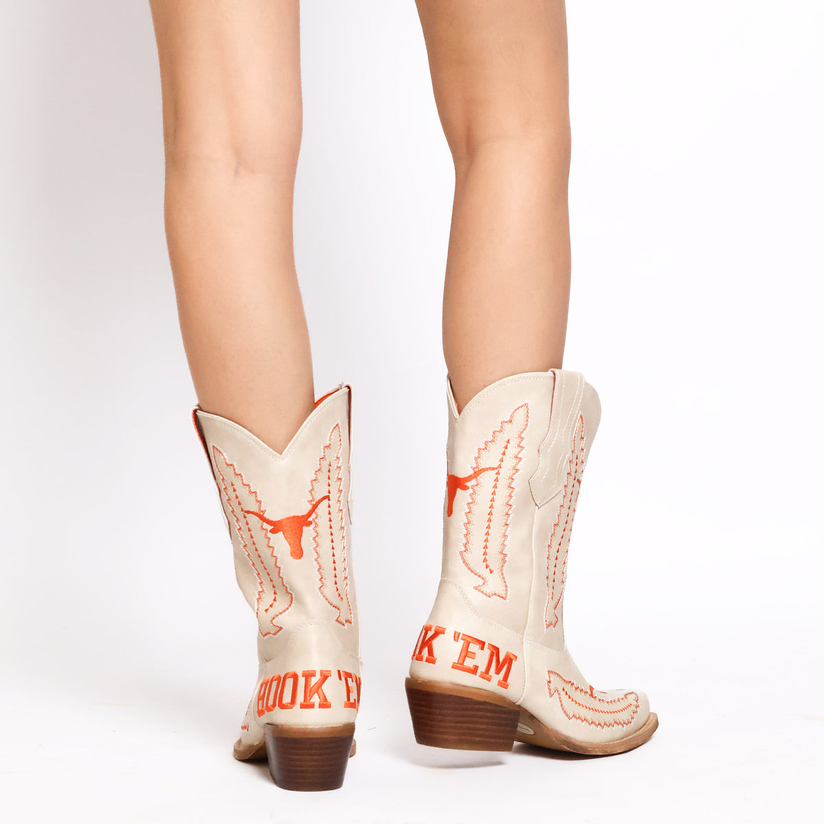Back view of cream cowboy boots with orange bull logo and stitched panels, wooden heel.